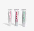 Moisturizing lip balm trio from Topicals Slick Salve in Açaí, Pomegranate, and Mint standing upright side by side on a white background.